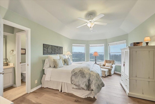 bedroom featuring light wood-type flooring, a raised ceiling, baseboards, and ensuite bathroom