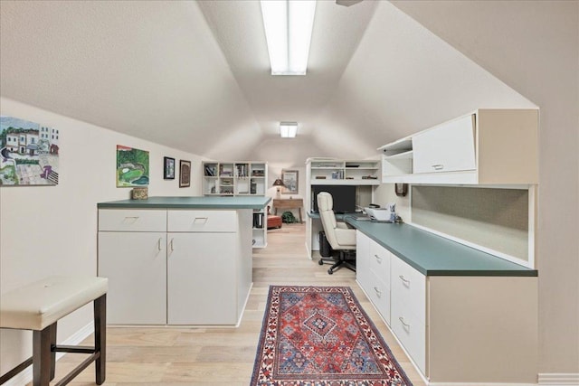 interior space featuring light wood-style floors, lofted ceiling, and built in desk