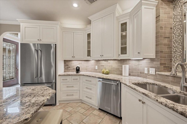 kitchen featuring arched walkways, appliances with stainless steel finishes, ornamental molding, a sink, and backsplash