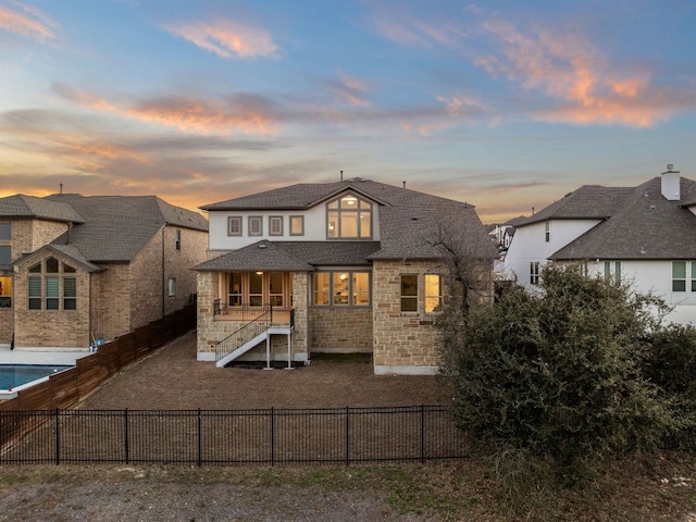 back of house with stone siding, a fenced backyard, and a fenced in pool