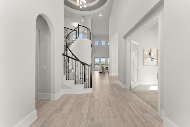 foyer with baseboards, stairway, wood finished floors, a high ceiling, and a chandelier