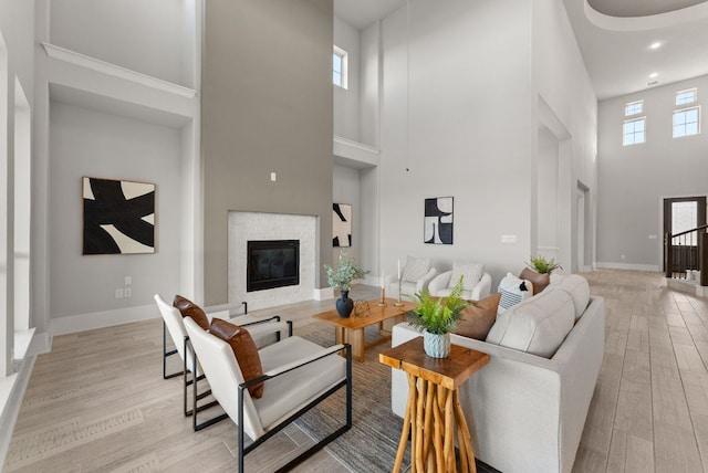 living area with baseboards, a glass covered fireplace, a towering ceiling, and light wood-style floors