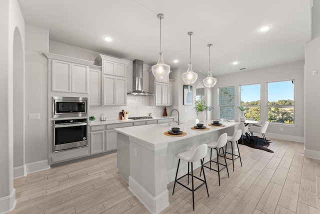 kitchen with appliances with stainless steel finishes, wood tiled floor, backsplash, and wall chimney range hood