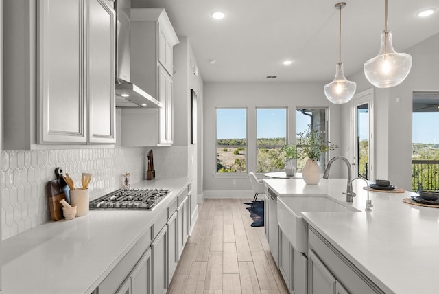 kitchen featuring decorative backsplash, light countertops, wall chimney range hood, stainless steel gas stovetop, and a sink