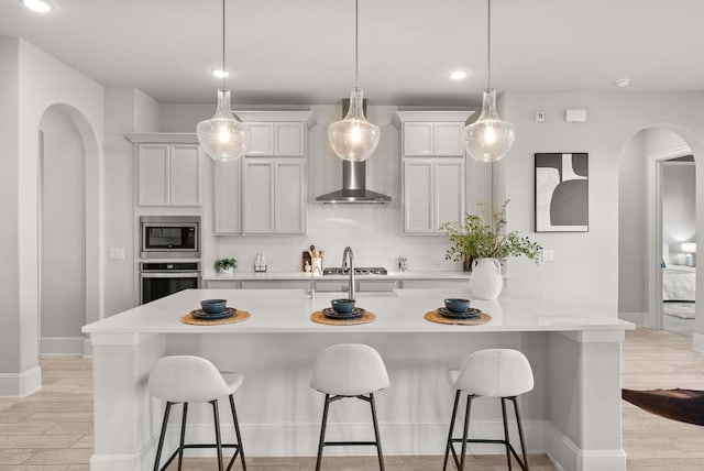 kitchen with stainless steel appliances, arched walkways, light wood-style flooring, and a breakfast bar