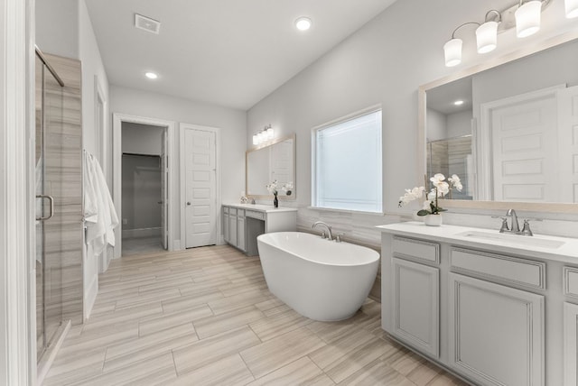 full bathroom with visible vents, a sink, a freestanding tub, a shower stall, and two vanities