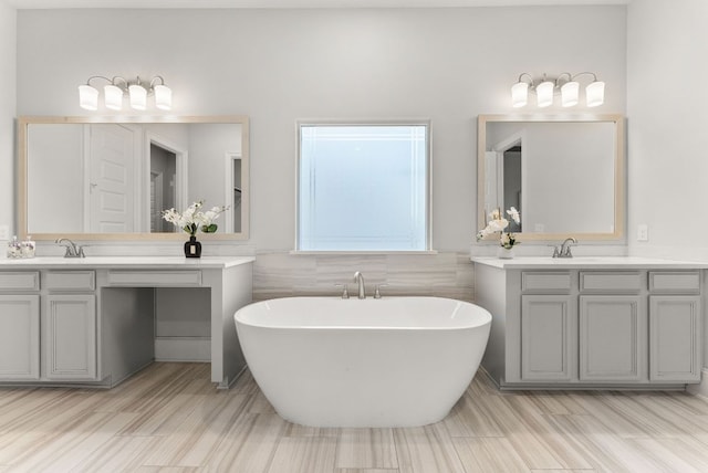 bathroom featuring a sink, a soaking tub, two vanities, and tile walls