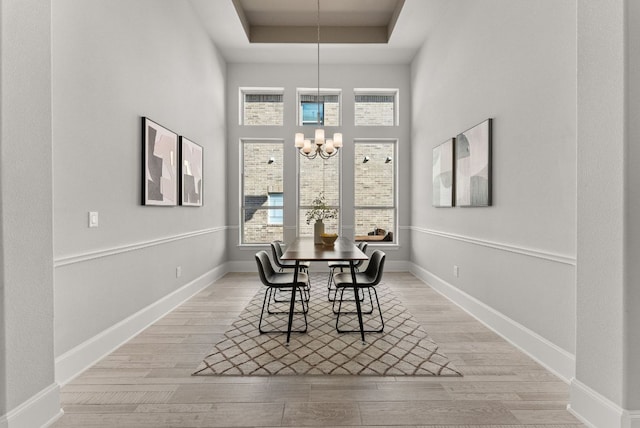 dining space with a chandelier, a tray ceiling, plenty of natural light, and light wood-style floors