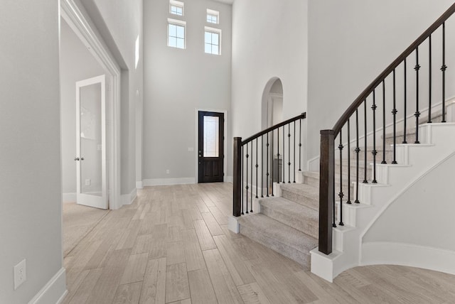 entrance foyer featuring a towering ceiling, baseboards, a wealth of natural light, and wood finished floors