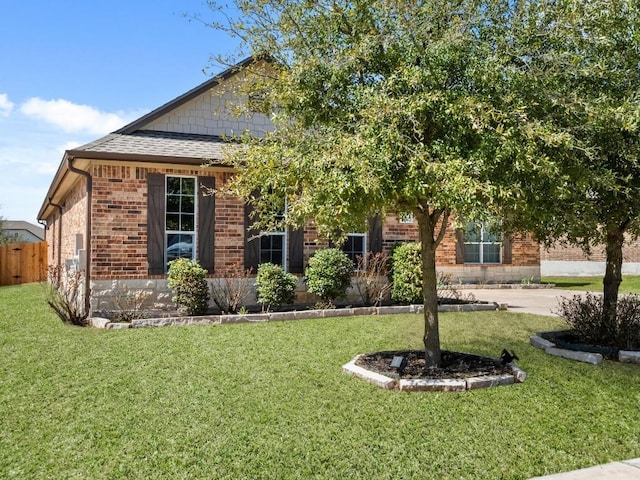 view of front of property featuring brick siding, fence, a front lawn, and roof with shingles