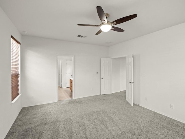 unfurnished bedroom featuring ceiling fan, connected bathroom, light carpet, visible vents, and baseboards