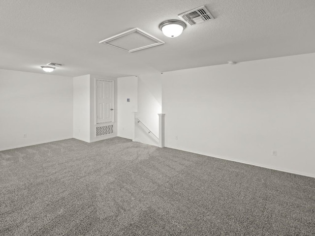 carpeted spare room with a textured ceiling, visible vents, and attic access