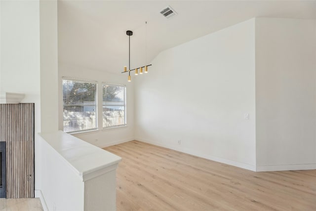 unfurnished dining area with a fireplace, lofted ceiling, visible vents, light wood-style flooring, and baseboards