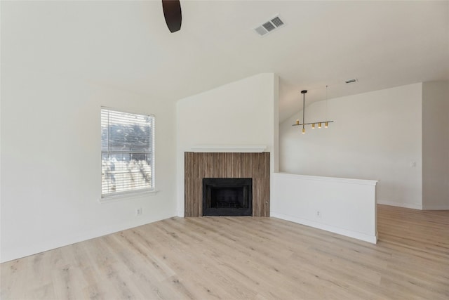 unfurnished living room with vaulted ceiling, visible vents, a fireplace, and light wood-style flooring