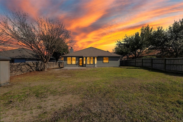 back of property at dusk with a fenced backyard, a patio, and a yard