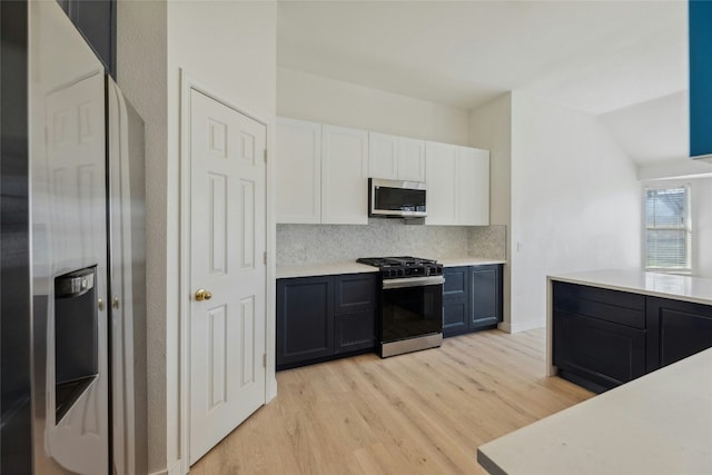 kitchen featuring white cabinets, light wood-style flooring, appliances with stainless steel finishes, light countertops, and backsplash