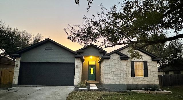 ranch-style house featuring concrete driveway, stone siding, an attached garage, and fence