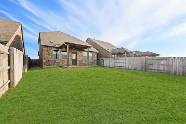 rear view of property featuring a fenced backyard, a yard, and brick siding