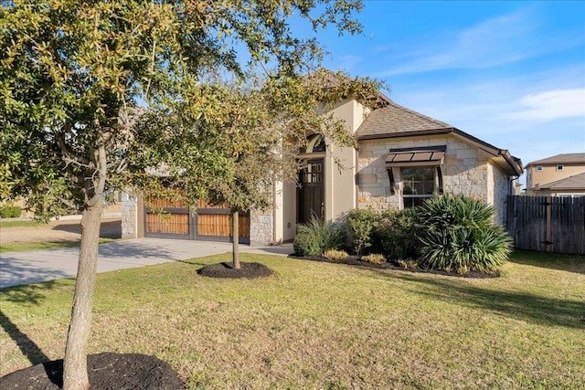 view of front of home featuring a shingled roof, fence, stone siding, driveway, and a front lawn