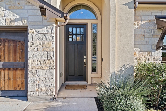 view of exterior entry with stone siding, fence, and stucco siding