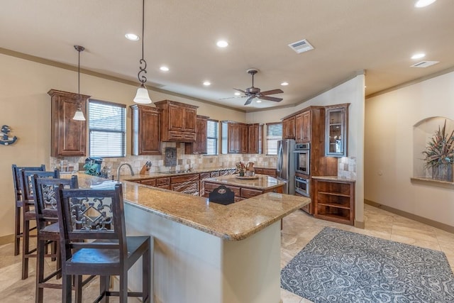 kitchen featuring light stone counters, tasteful backsplash, visible vents, a peninsula, and a kitchen breakfast bar