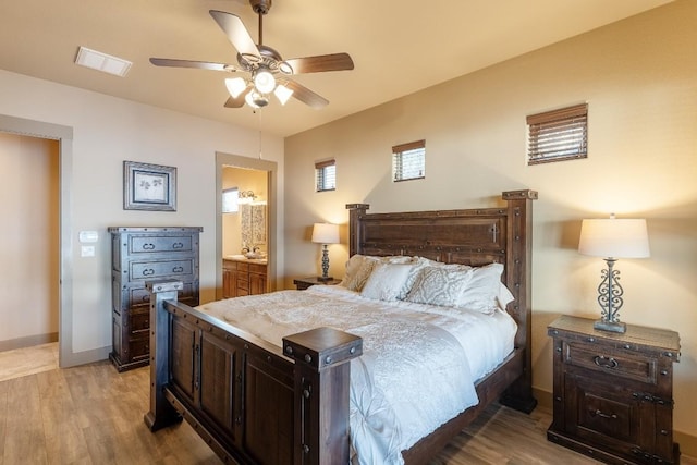 bedroom featuring light wood finished floors, baseboards, visible vents, a ceiling fan, and ensuite bath