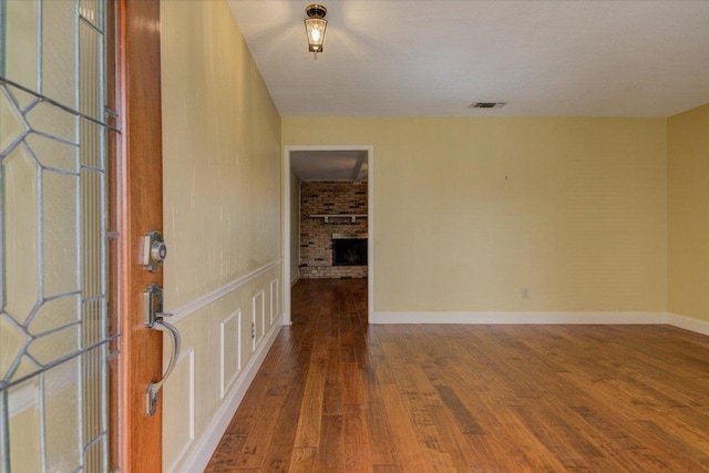 unfurnished room featuring a brick fireplace, visible vents, baseboards, and wood finished floors