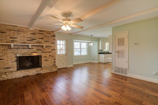 unfurnished living room featuring baseboards, a ceiling fan, wood finished floors, beamed ceiling, and a brick fireplace