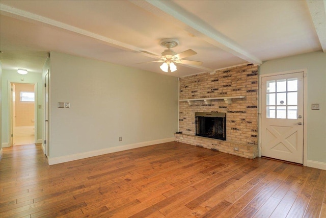 unfurnished living room featuring wood-type flooring, a ceiling fan, a brick fireplace, beamed ceiling, and baseboards