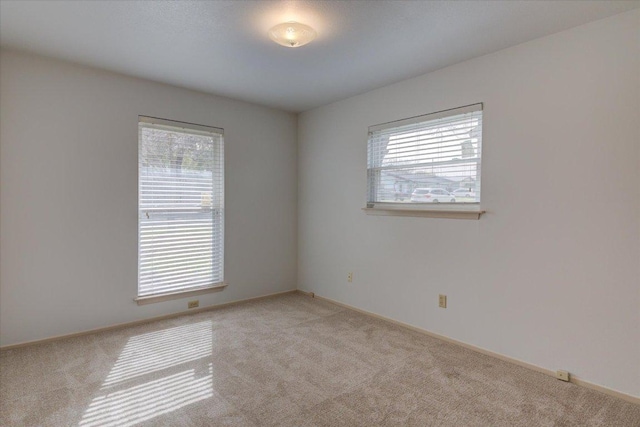 unfurnished room featuring a wealth of natural light, light carpet, and baseboards