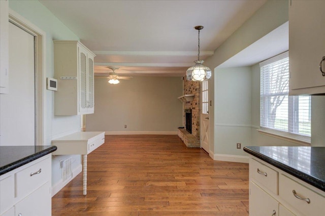 kitchen with glass insert cabinets, a fireplace, light wood-style flooring, and baseboards