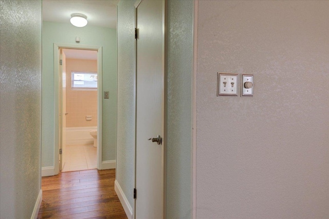 hallway with hardwood / wood-style flooring, baseboards, and a textured wall