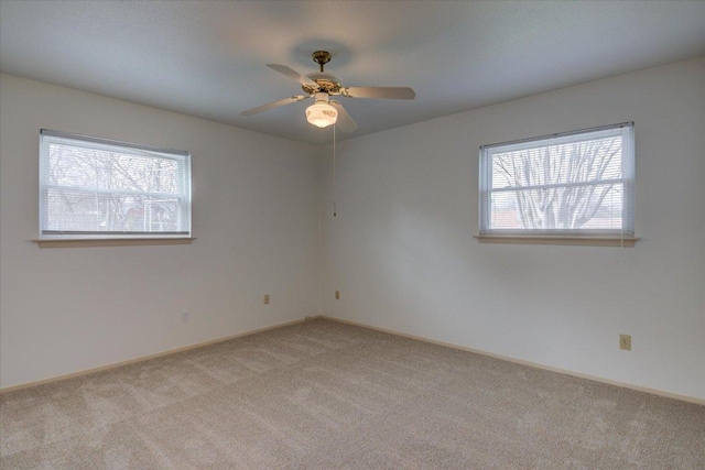 empty room featuring a ceiling fan, a wealth of natural light, light colored carpet, and baseboards