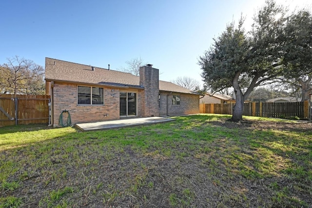 back of property with brick siding, a yard, a chimney, a patio, and a fenced backyard