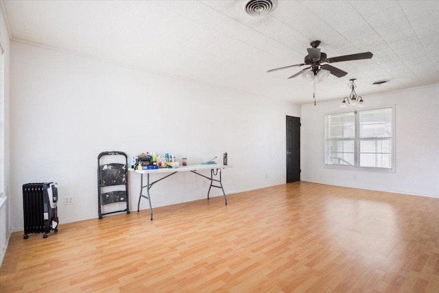 empty room featuring ceiling fan with notable chandelier, wood finished floors, visible vents, ornamental molding, and radiator heating unit