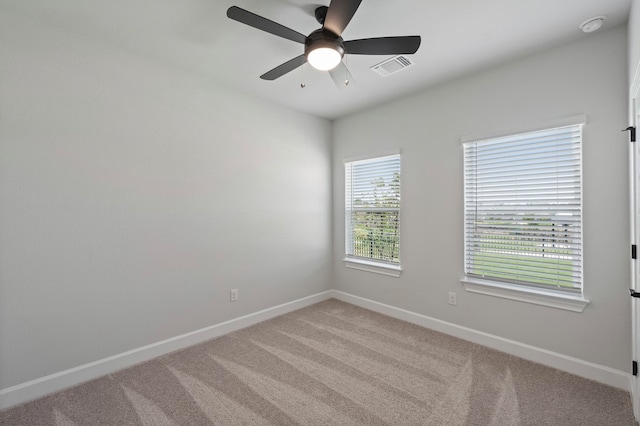 spare room featuring light carpet, a ceiling fan, visible vents, and baseboards