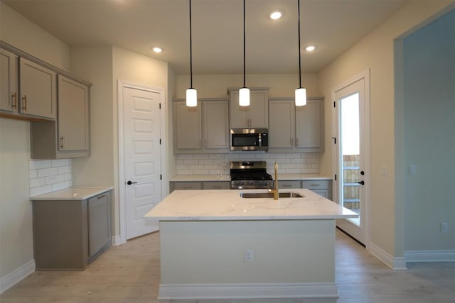 kitchen with tasteful backsplash, gray cabinetry, appliances with stainless steel finishes, a sink, and light wood-type flooring