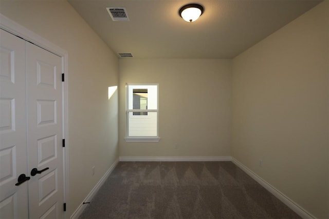 spare room with visible vents, baseboards, and dark colored carpet