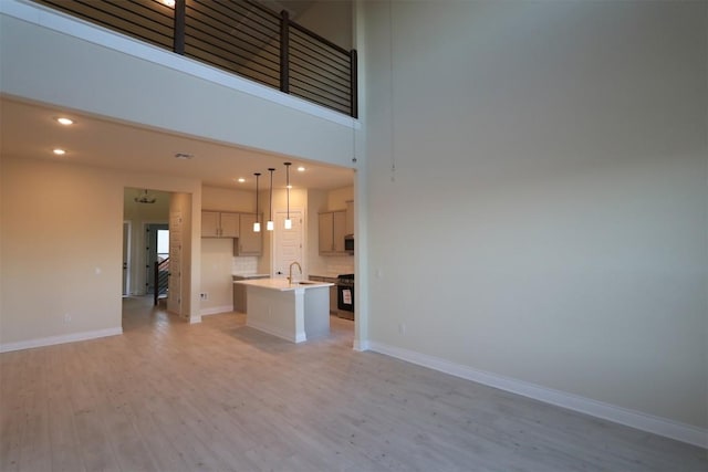 unfurnished living room with recessed lighting, light wood-style flooring, a high ceiling, and baseboards