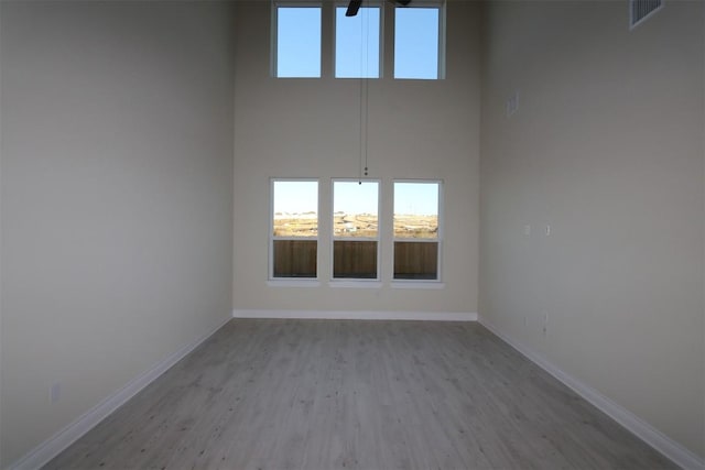 empty room featuring visible vents, baseboards, wood finished floors, and a towering ceiling