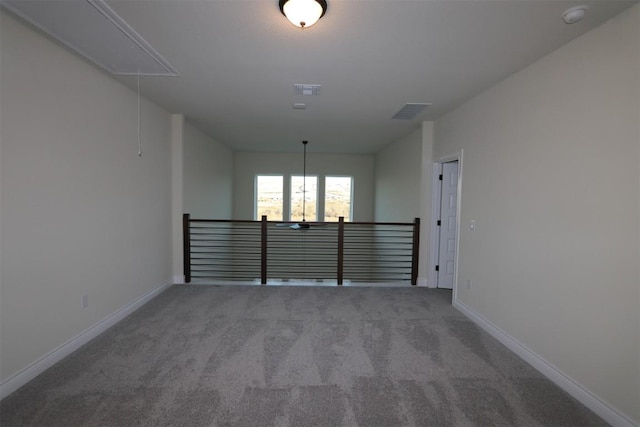 carpeted spare room with visible vents, baseboards, and attic access