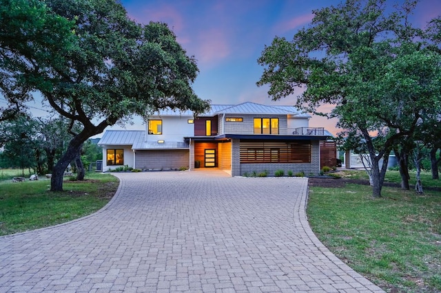 modern home with a standing seam roof, decorative driveway, a yard, and metal roof