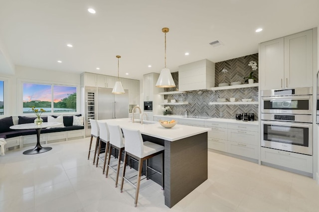 kitchen featuring backsplash, a breakfast bar area, light countertops, appliances with stainless steel finishes, and open shelves