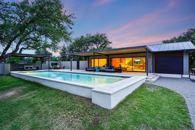 pool at dusk featuring a patio, a fenced in pool, fence, a lawn, and an outdoor hangout area