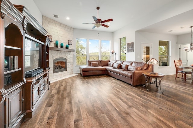 living area with a fireplace, visible vents, wood finished floors, and ceiling fan with notable chandelier