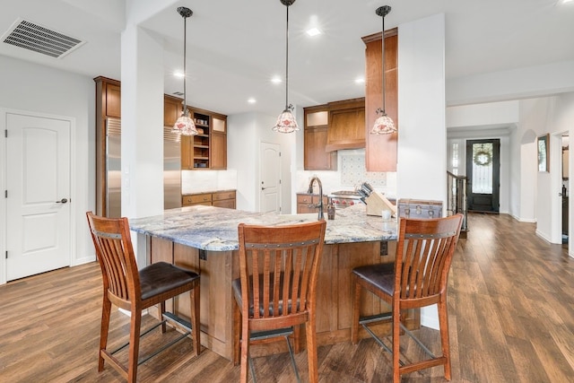 kitchen with visible vents, brown cabinetry, arched walkways, decorative backsplash, and a peninsula