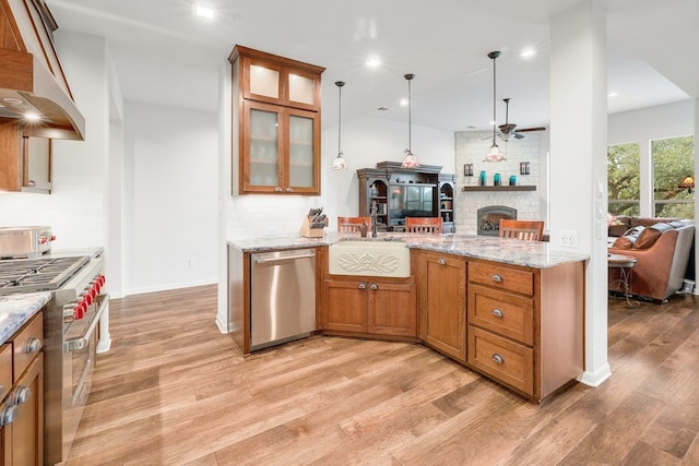 kitchen with light wood finished floors, appliances with stainless steel finishes, brown cabinets, under cabinet range hood, and backsplash