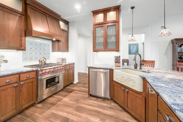 kitchen featuring brown cabinets, stainless steel appliances, custom range hood, a sink, and light wood-type flooring