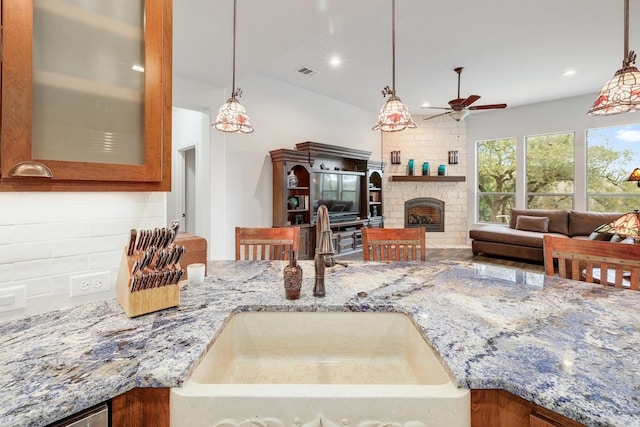 kitchen featuring a stone fireplace, stone countertops, a sink, visible vents, and backsplash