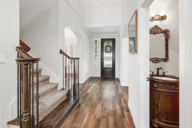 foyer entrance featuring dark wood-type flooring, arched walkways, stairway, and baseboards